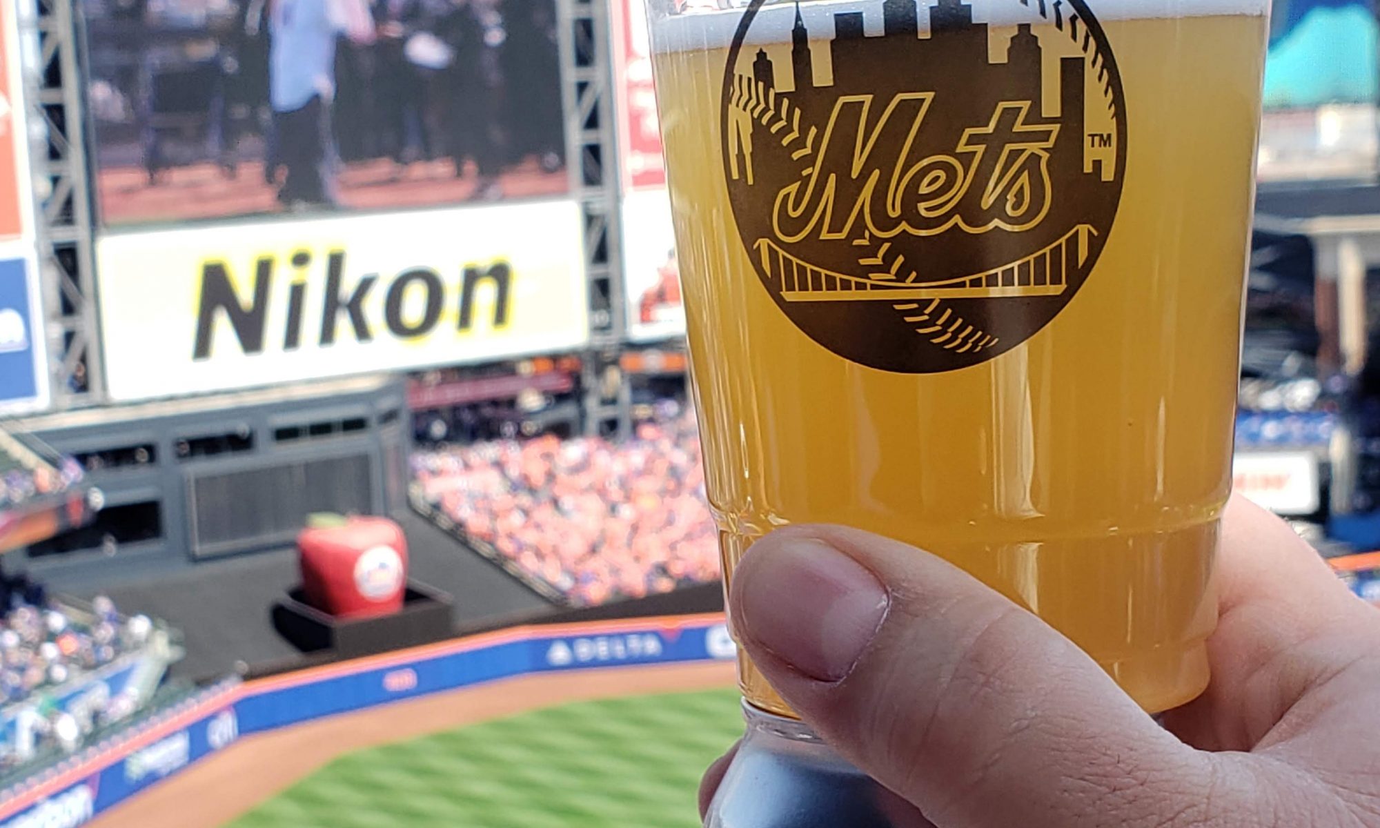 holding a NEIPA session ale in a Mets plastic cup at citi field up to the scoreboard with the field in the background