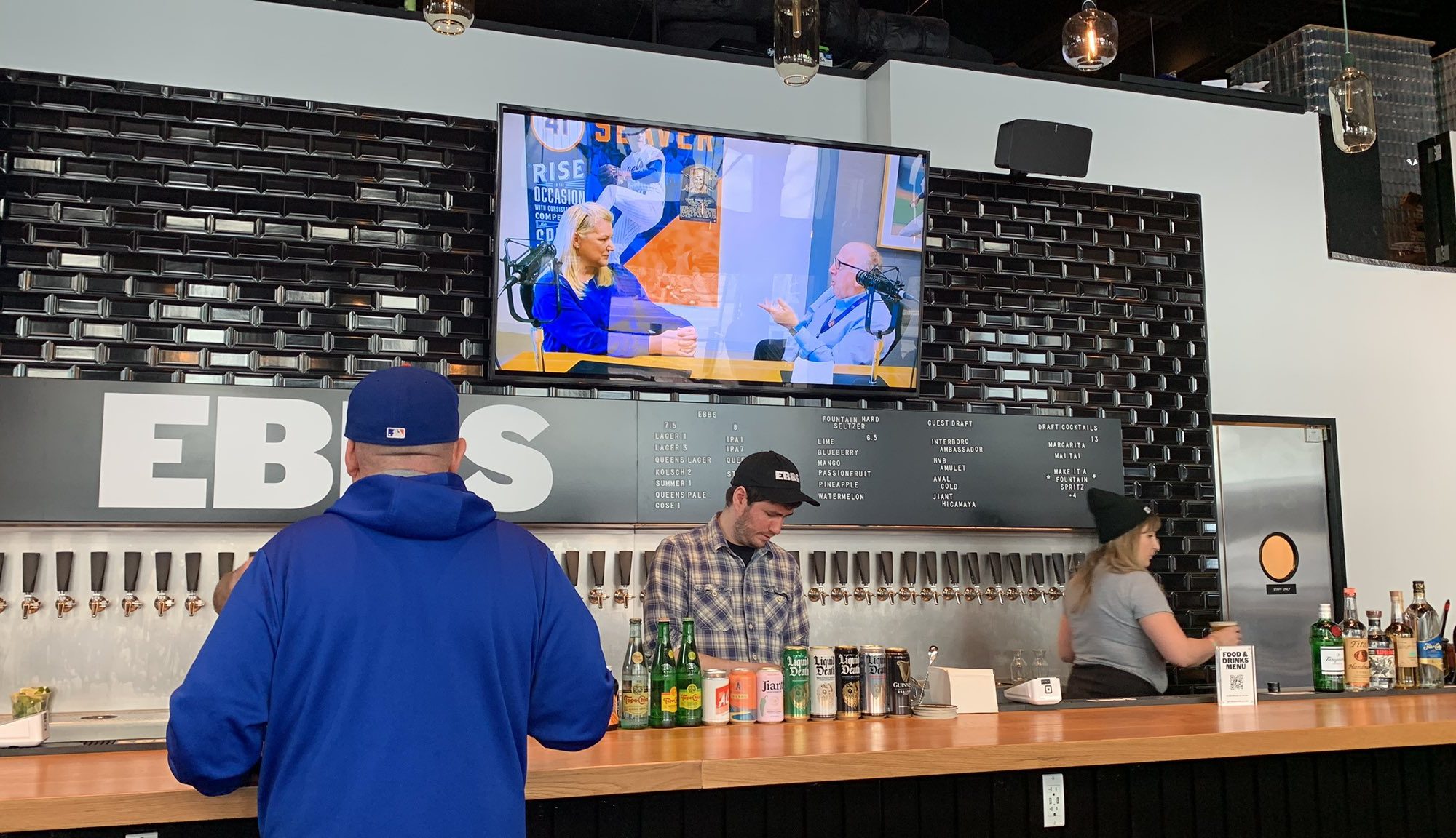 far shot of the Ebbs Citi Field bar, with a tv above the taps, and a few cans on the bar